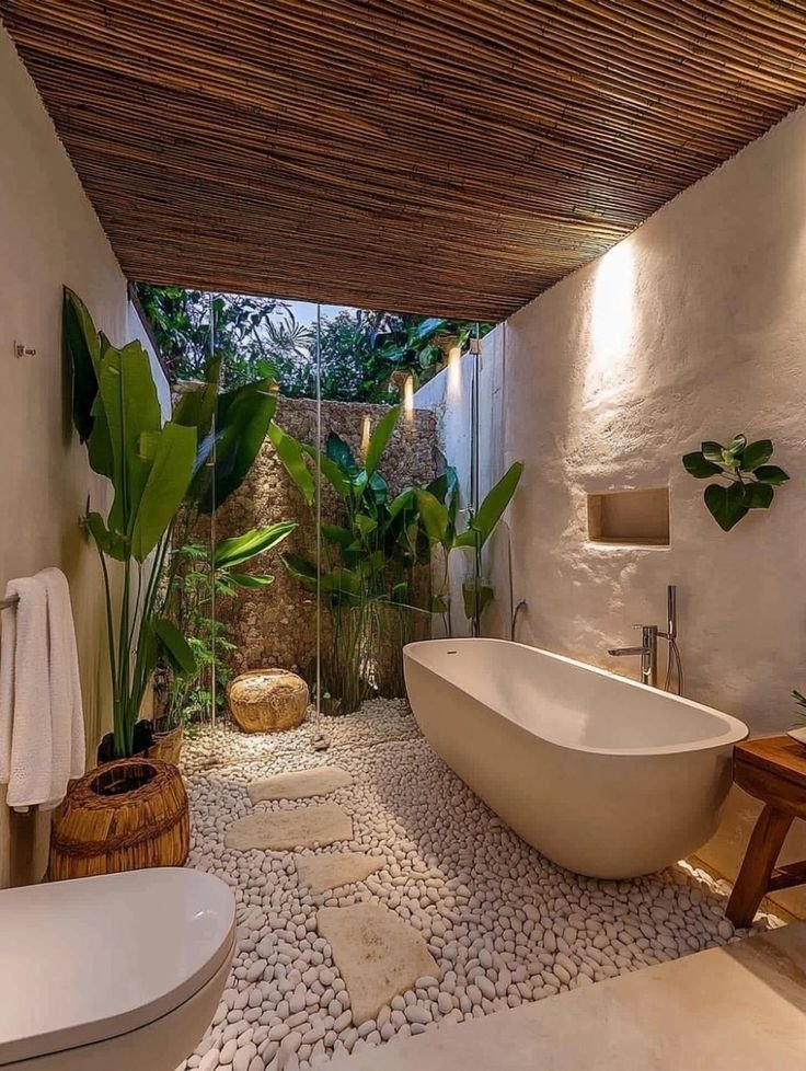 Outdoor luxury bathroom with white pebble stone flooring, freestanding bathtub, tropical plants, and bamboo ceiling design